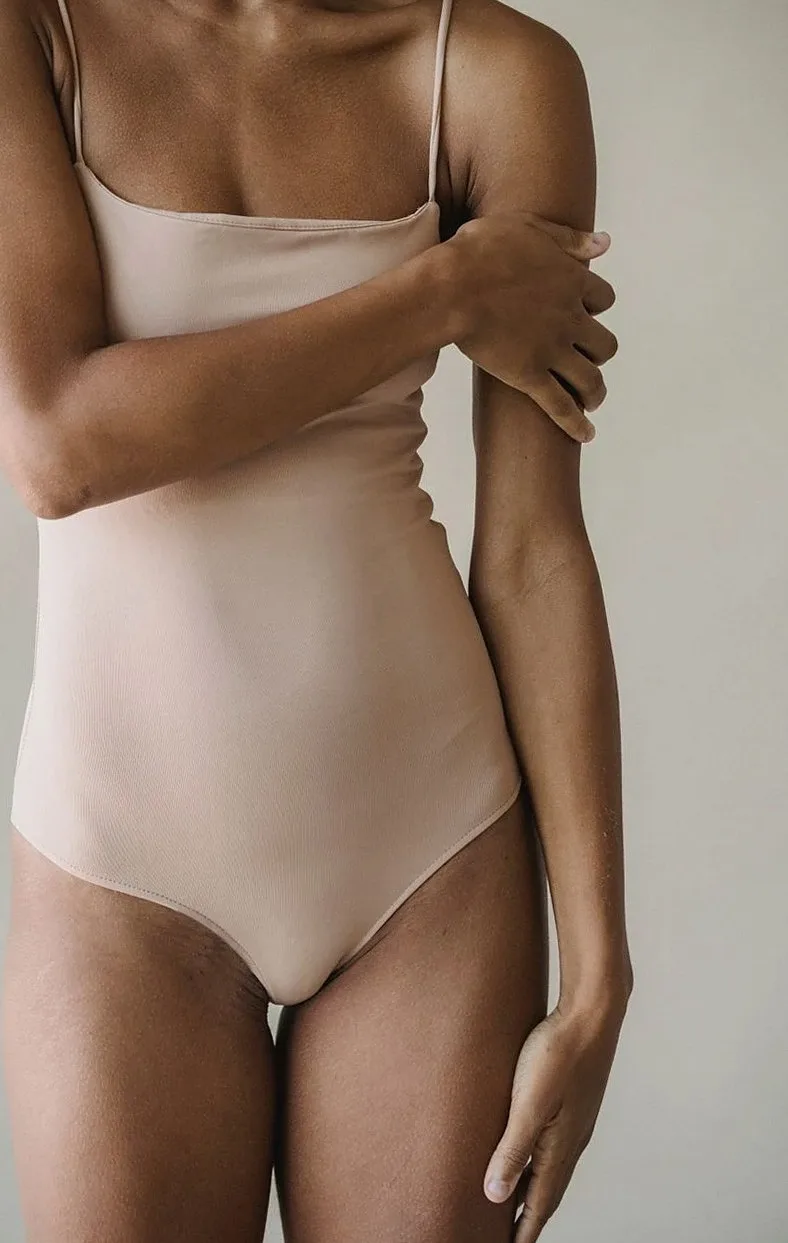 Nude-tone sculpting bodysuit worn by a model, shown from the shoulders down