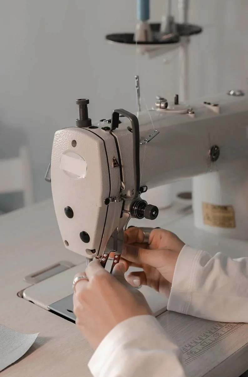 Close-up of a dressmaker using a sewing machine in a workshop, focusing on hands and details.